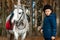 Boy in a jockey cap portrait, stands next to a white pony close-up on the background of nature. Jockey, epodrome, horseback riding