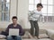 Boy Jumping On Sofa While Father Using Laptop At Home