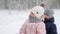 Boy and little girl in pink jumpsuit sledding on snowy winter day. Parents pull sled with son and daughter on snowfall