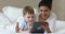 Boy lying on bed with Indian babysitter using digital tablet