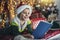 Boy lying on front on floor by christmas tree, reading book surrounded by gifts