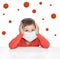 A boy in a medical mask holds on to his head. Around the viruses