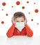 A boy in a medical mask holds on to his head. Around the viruses