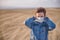 Boy in a medical mask outdoors closes his hands over his ears