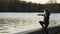 A boy in a medical mask on the shore throws stones into the water at sunset in slow mo