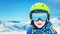 Boy with modern ski green helmet, yellow glasses and blue jacket. Reflection of snowy peaks on glasses