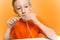 Boy in an orange T-shirt bites a strip of thin multicolored paper