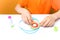 Boy in an orange T shirt sits at a white table and adjusts the twisted thin paper strips with his fingers performs crafts in the