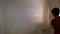 The boy paints the wall with white paint roller. Video picture. Shot from behind.