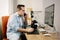 Boy photographer answering the phone while working from home on his computer. On the table are an electronic graphics tablet and a