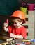 Boy play as builder or repairer, work with tools. Kid boy in orange hard hat or helmet, study room background. Childhood