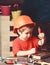 Boy play as builder or repairer, work with tools. Kid boy in orange hard hat or helmet, study room background. Childhood
