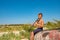 A boy is playing on a black clarinet sitting on an old wooden boat on the beach.