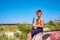 A boy is playing on a black clarinet sitting on an old wooden boat on the beach.