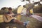 Boy playing guitar while father setting up a tent in background