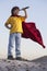 Boy playing superheroes on the sky background, teenage superhero in a red cloak on hill