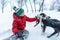 Boy plays with pets dogs in winter park. Teenager in knitted hat sits in the snow and caress mongrel dog