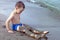 A boy plays on the seashore with sand. The child laid sand on his feet.