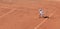 A boy plays tennis on a clay tennis court. The child is concentrated and focused on the game. Determined young athlete