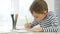 A boy of preschool age, drawing with colored pencils, sitting at a table, sitting by the window. Thoughtful, intelligent