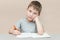 The boy preschool sits at a table with a pen and notebook. The child learns to write. The idea is preparing for school, completing