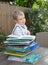 Boy preschooler sits at a table in the garden, in front of him is a large pile of children`s books