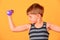 A boy with purple dumbbells goes in for sports and does physical exercises in the studio on a yellow background
