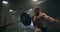 The boy pushes the barbell in the gym with one hand. An athlete without a T-shirt in a dark room lifts the barbell while