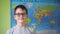 the boy puts on and adjusts his glasses standing against the background of the political map of the world. a smile on