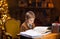 Boy reads a magic book while sitting at the table. Home interior with Christmas tree and fireplace. Traditional