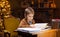 Boy reads a magic book while sitting at the table. Home interior with Christmas tree and fireplace. Traditional