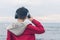 A boy in a red jacket and headphones looks at the sea waves in stormy weather