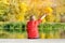 Boy in red jacket with leaves in hands sitting on the dock. Autumn, sunny. View from the back