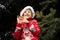 A boy in a red knitted Christmas sweater with a Christmas reindeer and a Santa Claus hat makes faces and gestures with his hands