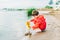 Boy in a red raincoat pours water out of yellow rubber boot into the lake. Child playing with water at pond. Kid having