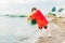 Boy in a red raincoat pours water out of yellow rubber boot into the lake. Child playing with water at pond. Kid having