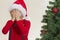 Boy in red Santa cap hidding his face with both hand near christmas tree