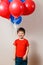 Boy in a red shirt holding helium balloons and laughing, eyes closed