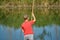 A boy in a red shirt throws a fishing rod on the catch river