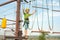 The boy is resting from overcoming obstacles in the sports park, holding the side ropes