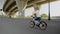 Boy rides white bicycle with spinning windmill on city road near high overpass bridge