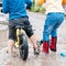 Boy is riding a bike and girl is riding a scooter across deep puddle