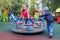 boy rolls girl in pink jacket on carousel in yard at playground outdoors