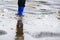 Boy in rubber blue rainboots jumping to dirty puddle