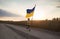 Boy runs along country road with yellow-blue Ukrainian large flag past wheat field