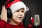 Boy in Santa Claus hat and headset is singing or talking into microphone with pop filter in voice recording studio.