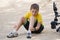 A boy with a scratched face sits on the ground and examines his wounds on his leg