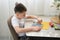 Boy sculpts figures from plasticine, sitting at home at the table. He is passionate about his hobby