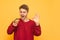 Boy shows an OK sign and looks at the burger in his hand, isolated on a yellow background. Hungry guy eats fast food. Student eats