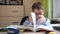 the boy shows a trick with a book. a teenager with glasses is doing homework. textbook and writing materials on the